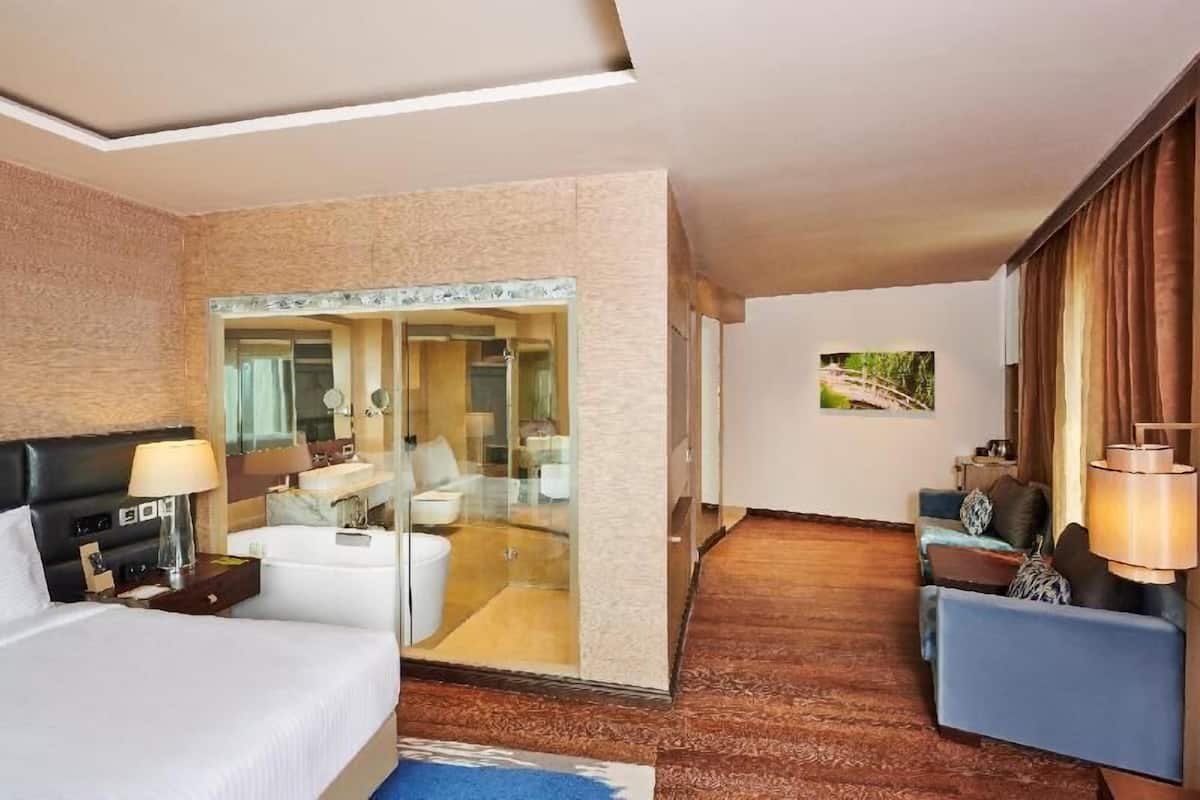 A hotel room with a bed, bedside table, lamp, and a glass-enclosed bathroom.