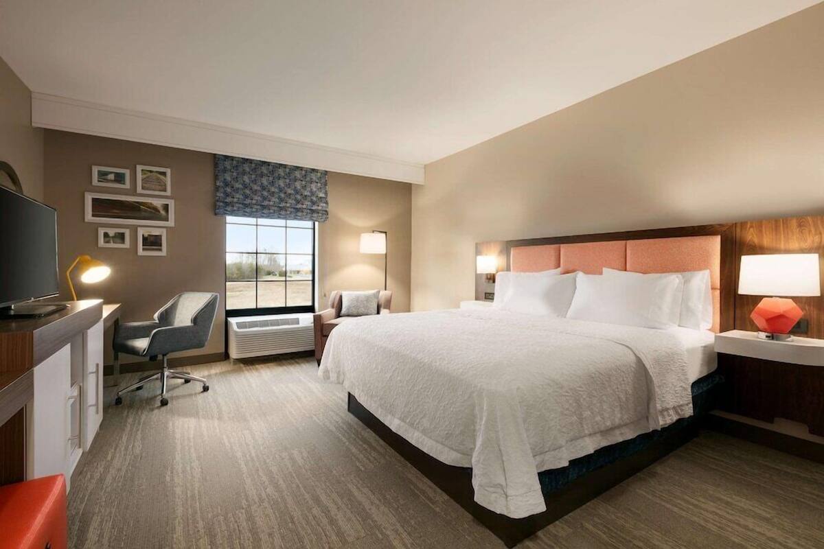 A hotel room with a large bed, a desk with a computer, a chair, a window with a view, and a TV.