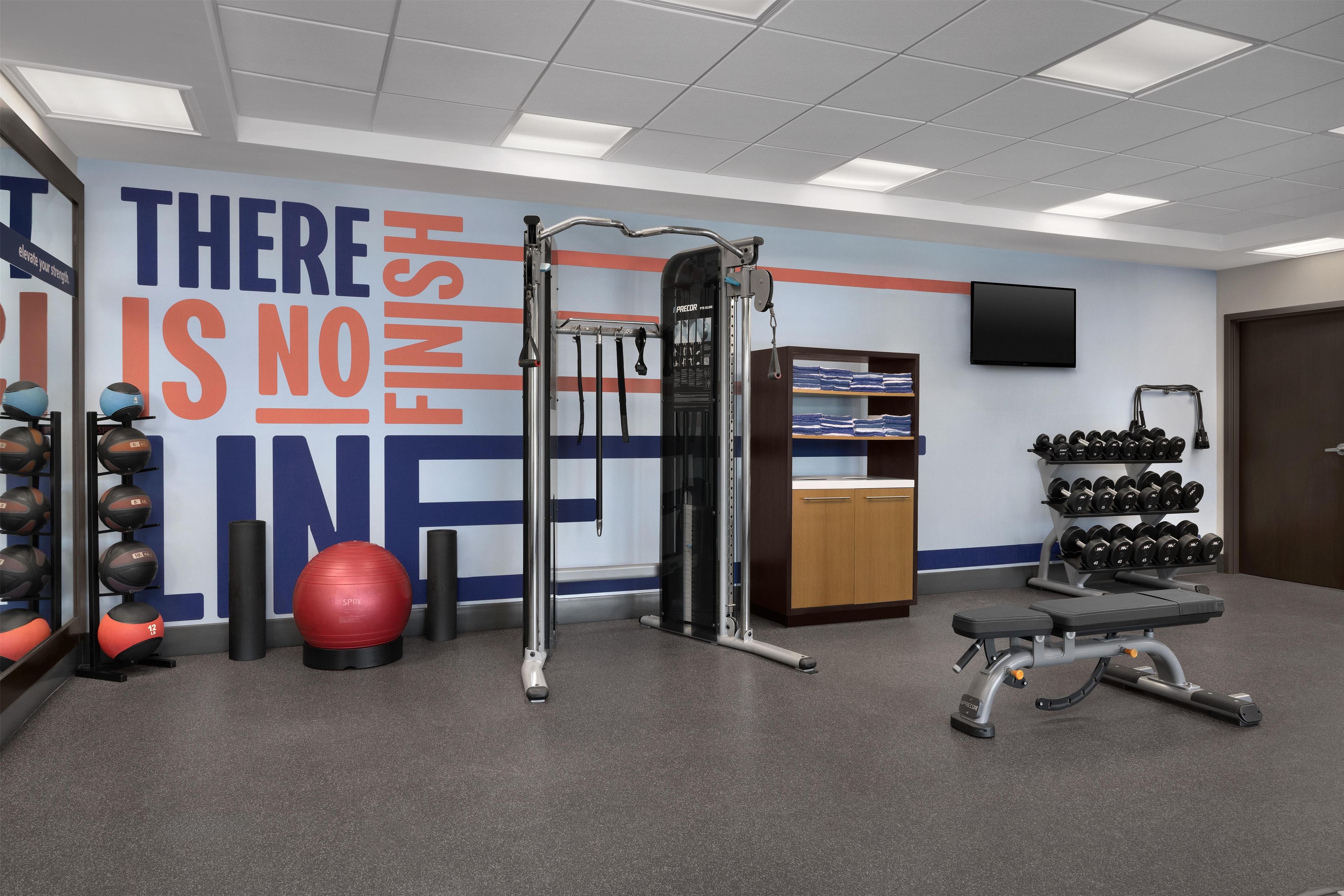 A gym with exercise equipment, a motivational wall, and a wall-mounted TV.