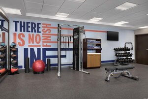 Un gimnasio con equipo de ejercicio, una pared motivacional y un televisor instalado en la pared.