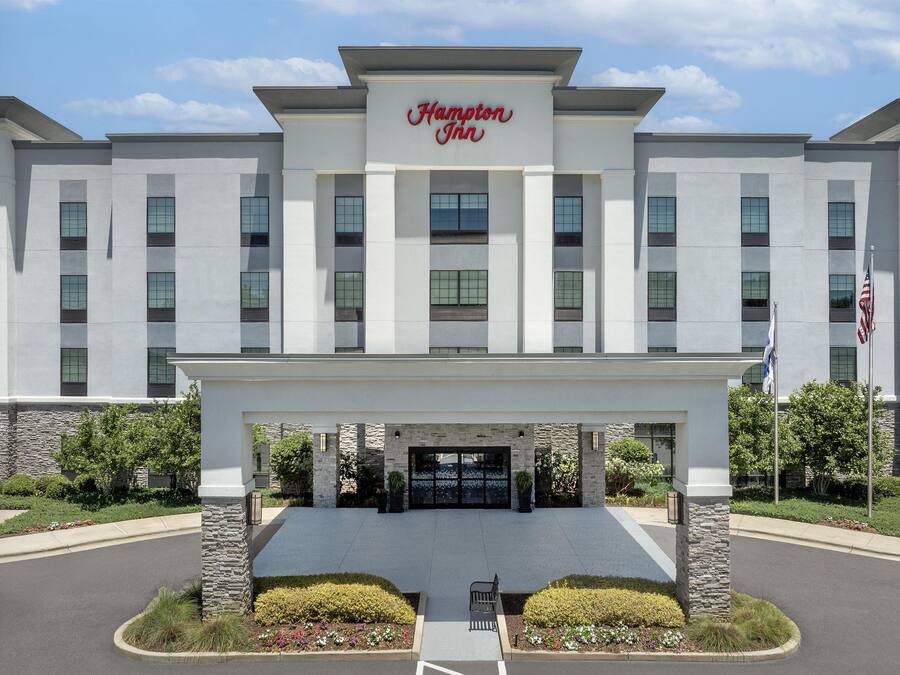Un hotel Hampton Inn con facciata moderna, ingresso centrale e giardino anteriore curato.