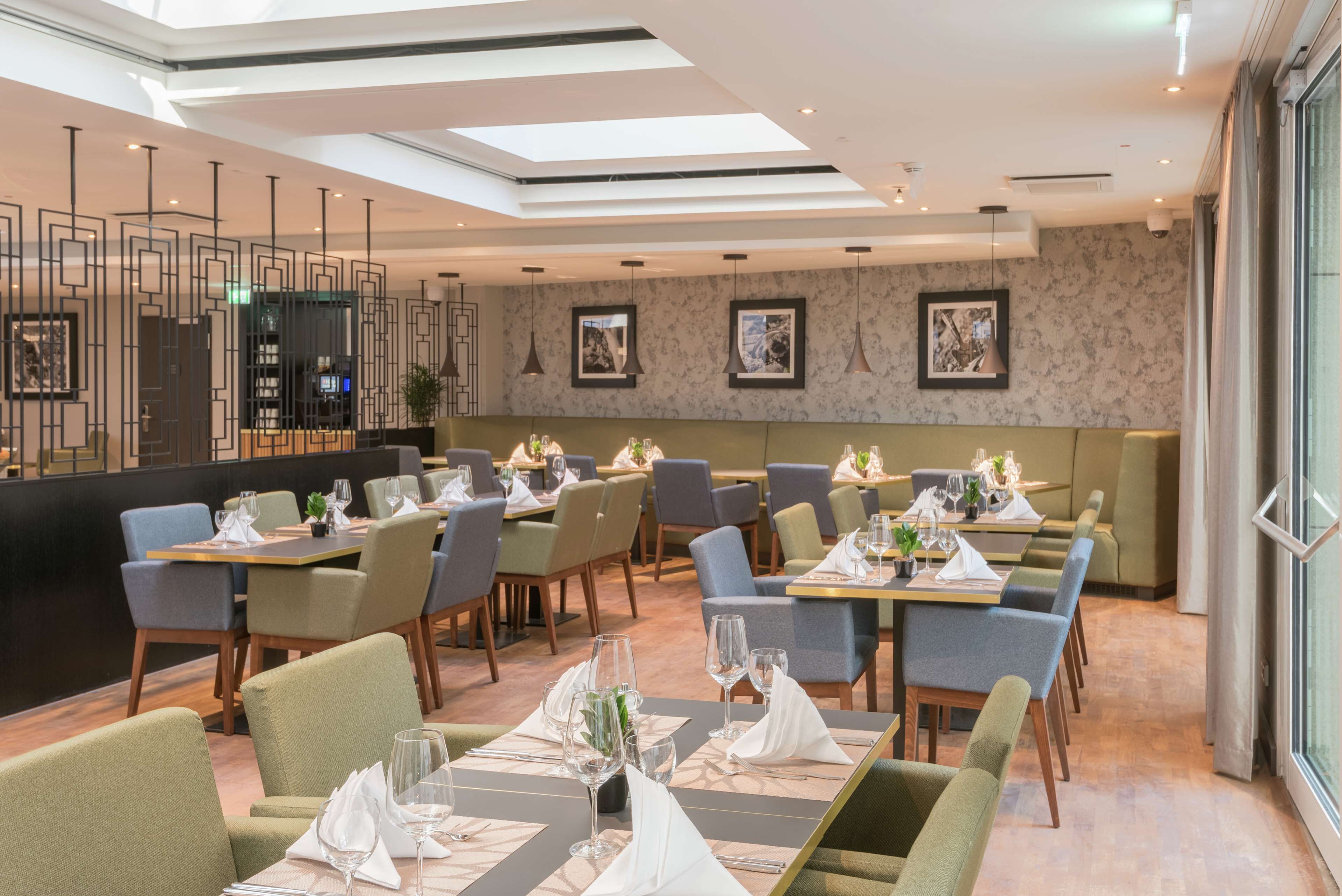 Un restaurante moderno con mesas y sillas ordenadas, un techo alto con tragaluces y obras de arte enmarcadas en las paredes.