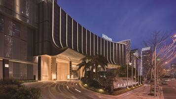 A modern hotel with a curved facade, illuminated signage, and a landscaped entrance area.