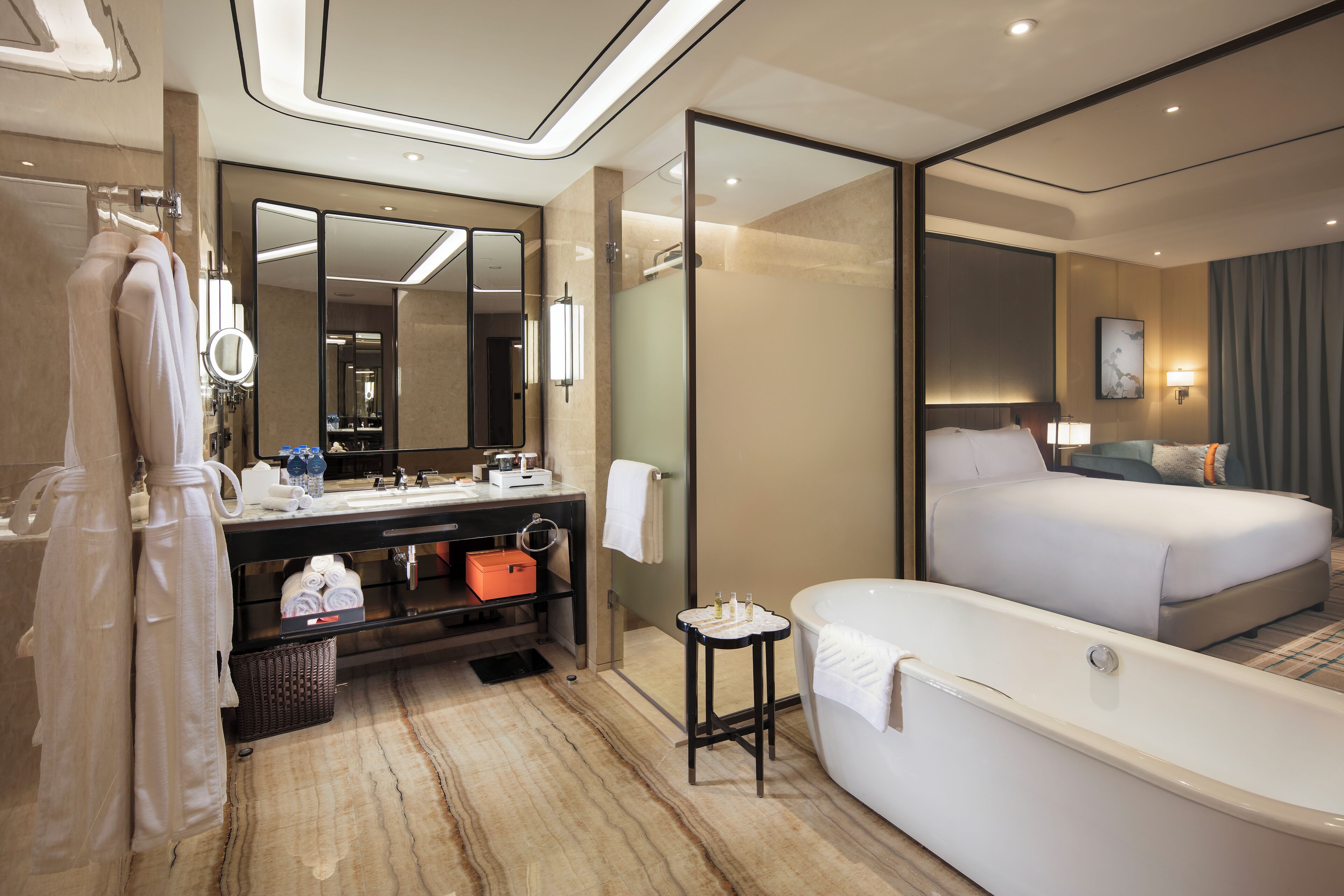 A modern hotel room with a large bed, a separate bathroom with a bathtub, a vanity with a mirror, and a small table with toiletries.