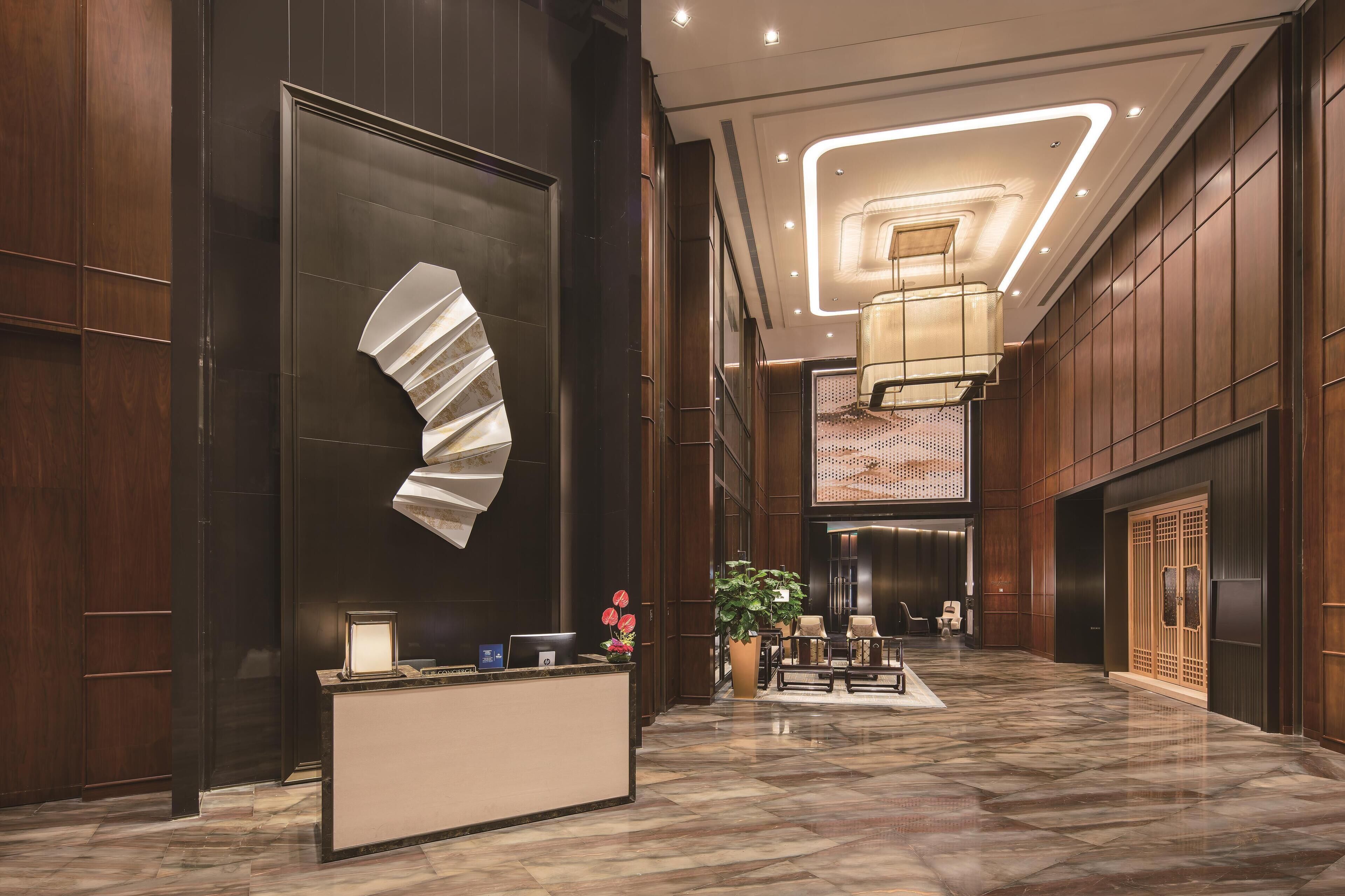 A modern hotel lobby with a reception desk, seating area, and a large decorative wall piece.