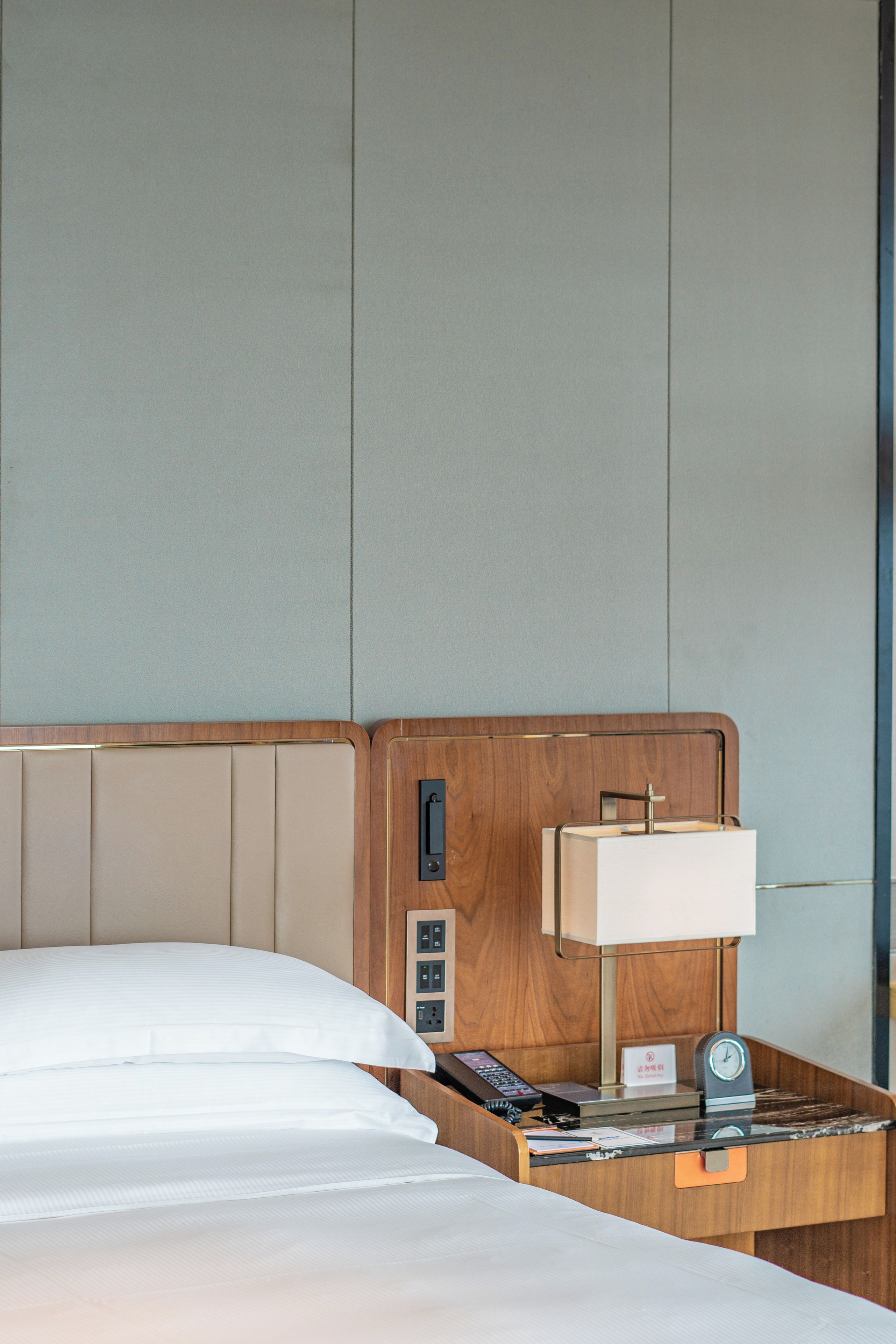 Een hotelkamer met een bed, een nachtkastje met een lamp, een klok en een 'Niet roken'-bord.