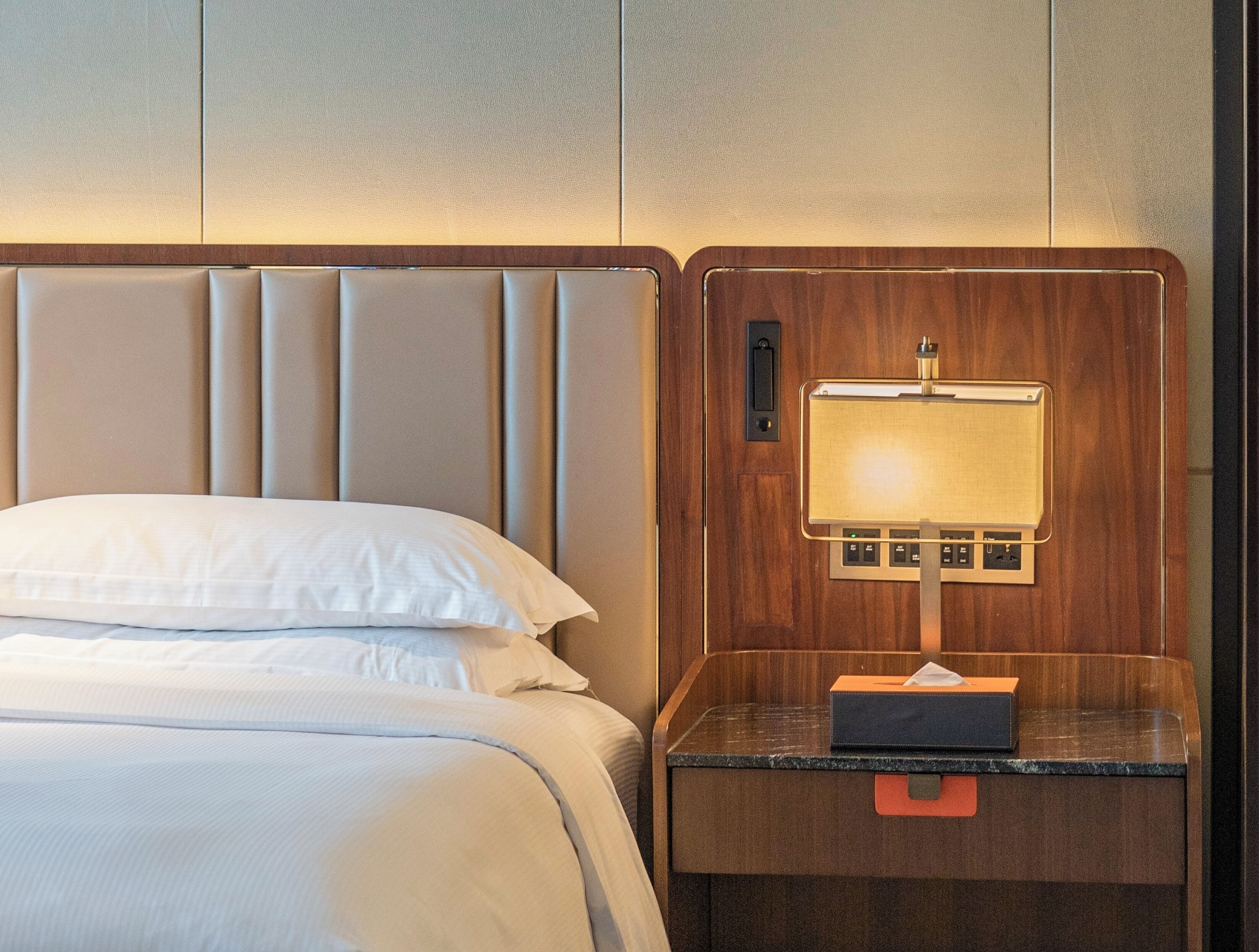 Una habitación de hotel con una cama, una mesita de noche con lámpara y un cabecero de madera.