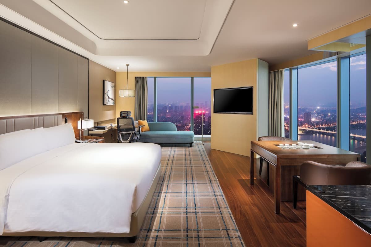 A hotel room with a large bed, a desk with a chair, a sofa, and a TV.