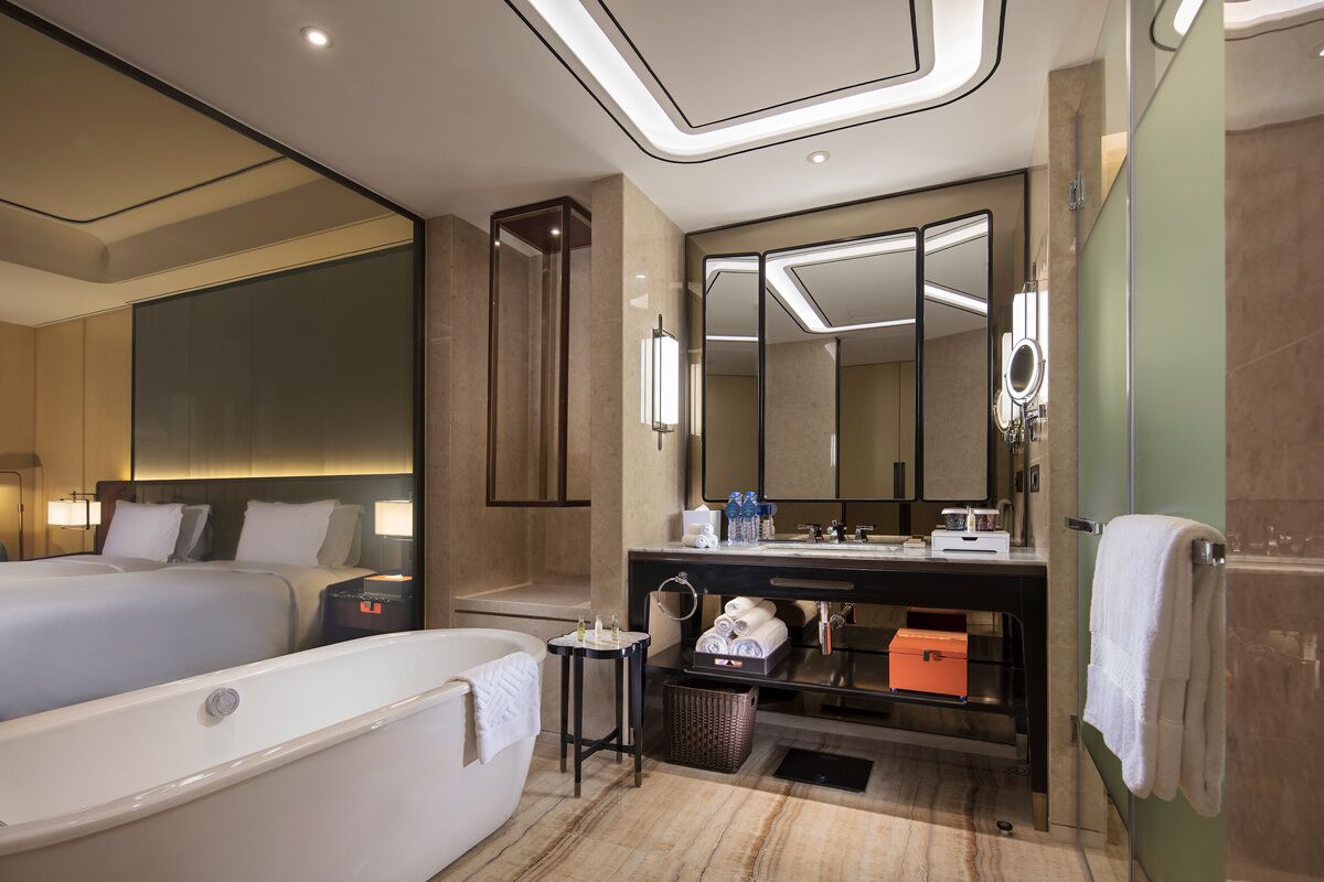 Ein Hotelzimmer mit einem großen Bett, einem separaten Badezimmer mit Badewanne, einem Schminktisch mit Spiegel und einem großen Spiegel über dem Schminktisch.