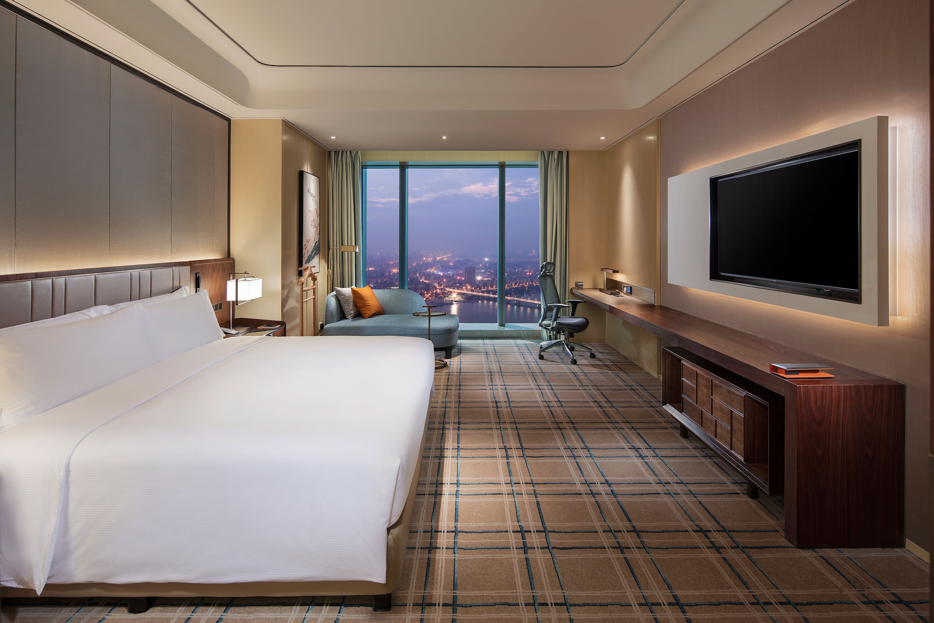 A hotel room with a large bed, a sofa, a desk, and a TV.