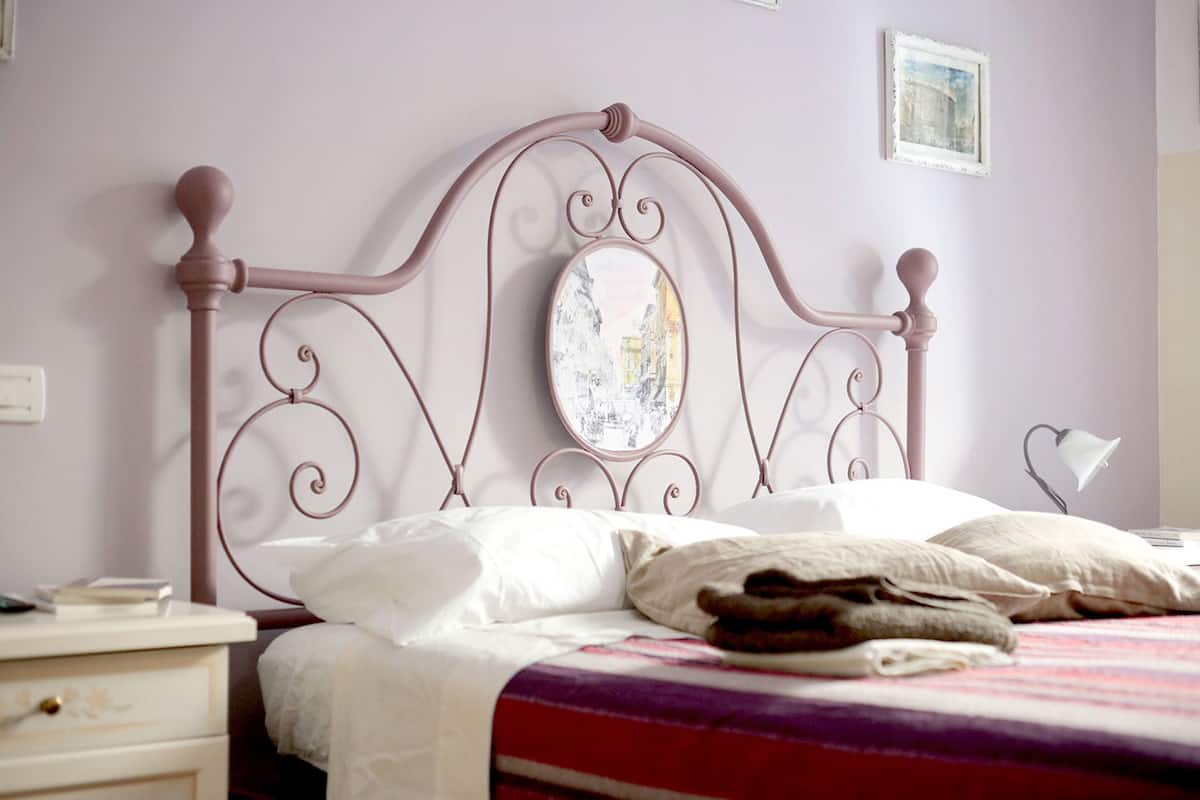 Uma cama bem arrumada com cabeceira de metal, uma mesa de cabeceira com abajur e um quadro na parede.