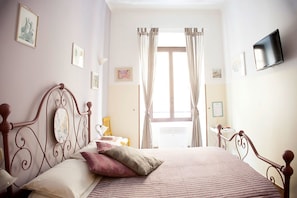 Un dormitorio con cama, cortinas, televisor y cuadros en la pared.