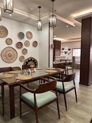 A dining area with a wooden table set for four, surrounded by chairs with green cushions. - Makarim Al Nakheel serviced apartments (Rabigh)