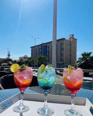 Three cocktails on a table with a view of a tall building and a clear sky. - Makarim Al Nakheel serviced apartments (Rabigh)