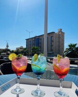 Three cocktails on a table with a view of a tall building and a clear sky.