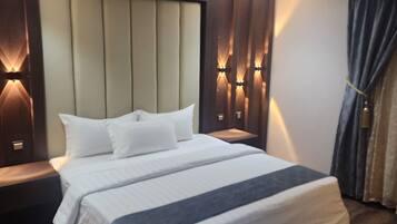 Quarto de hotel moderno com uma cama grande, piso de madeira e iluminação embutida na parede.