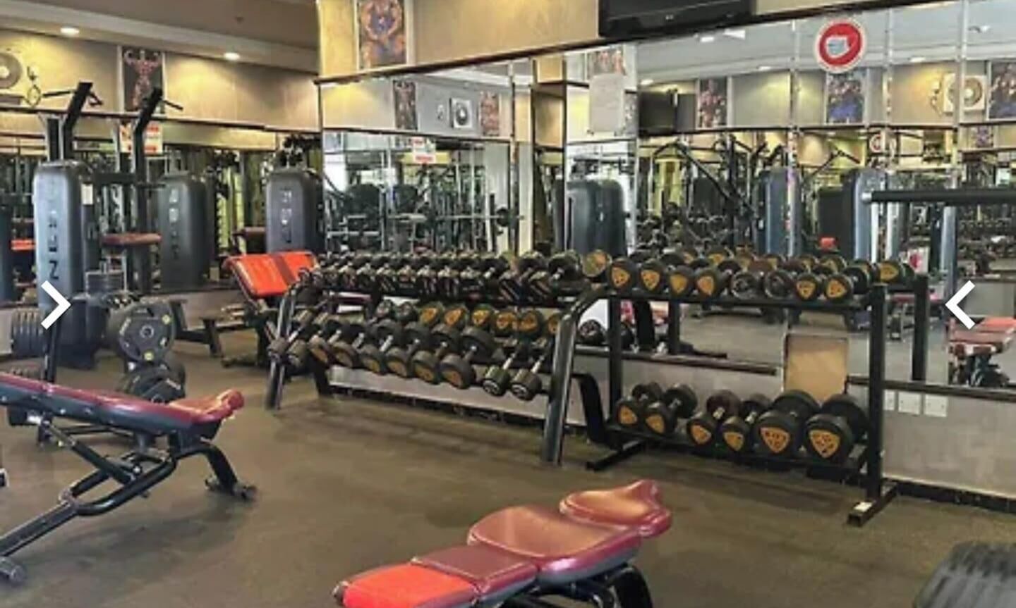 Un gimnasio con equipo de levantamiento de pesas, bancos y un espejo grande.
