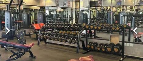 Un gimnasio con equipo de levantamiento de pesas, bancos y un espejo grande.