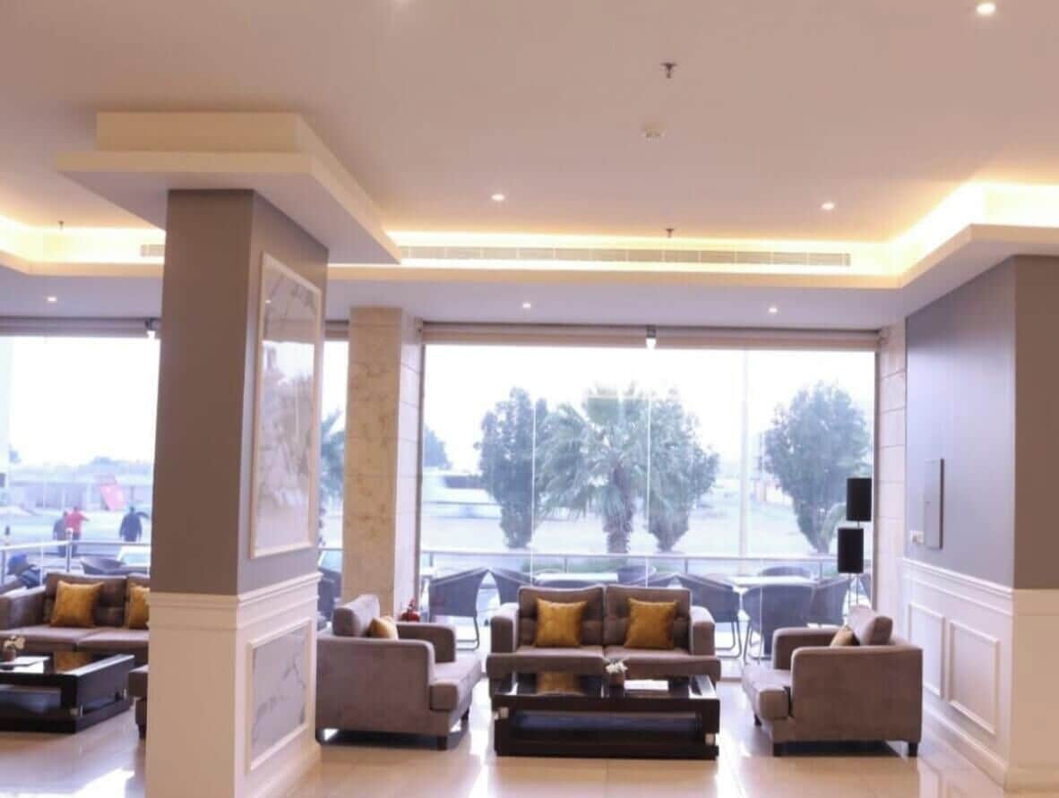 A spacious lobby with a large window, multiple seating areas, and a modern ceiling design.