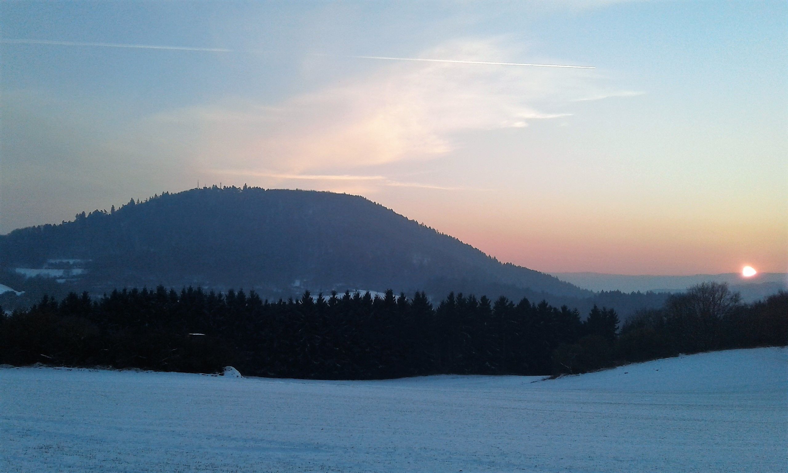 A snowy landscape with a mountain and a forest.