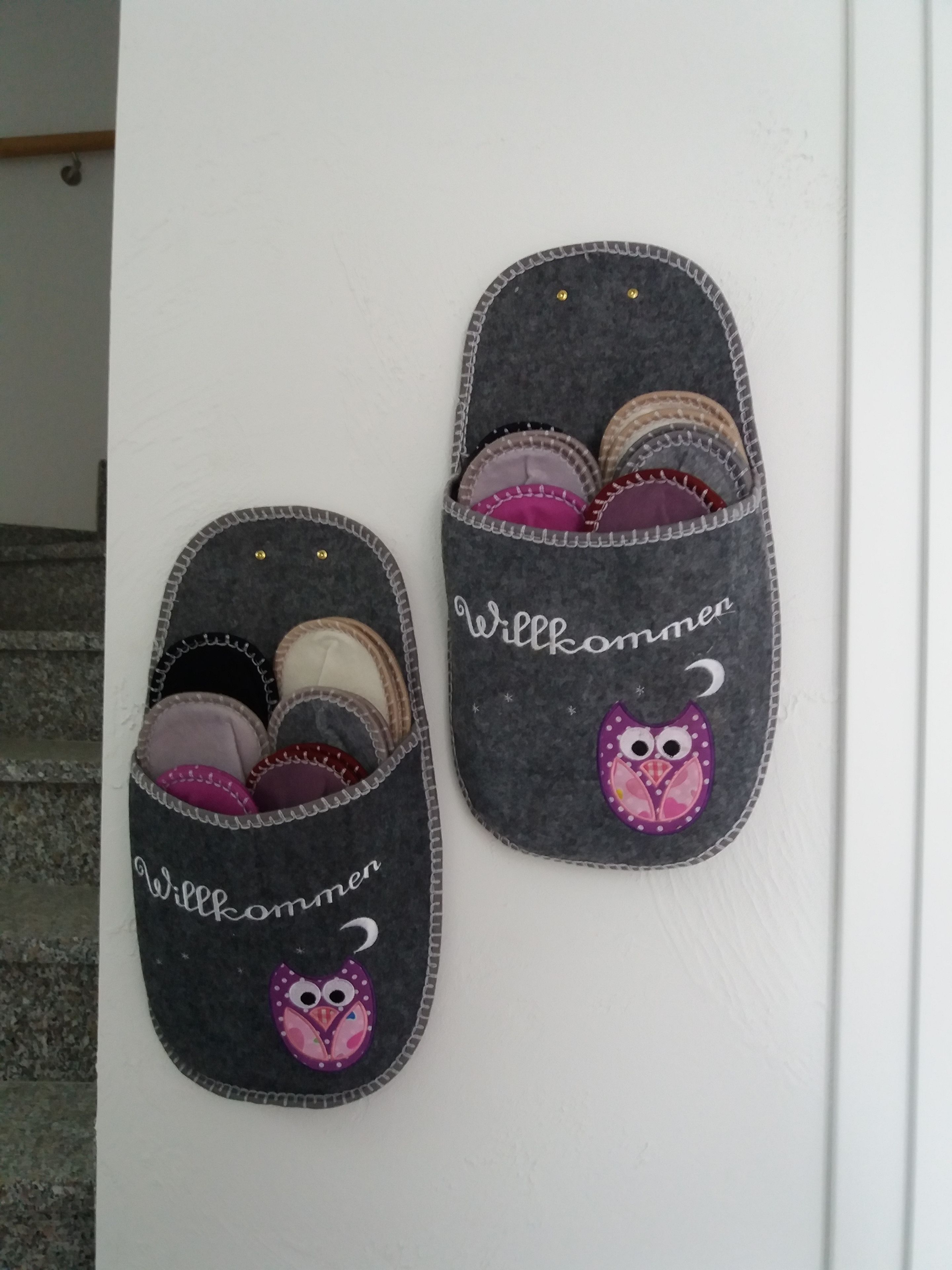 Un par de pantuflas con el texto "Willkommen" y un diseño de búho, probablemente para un hotel o habitación de huéspedes.