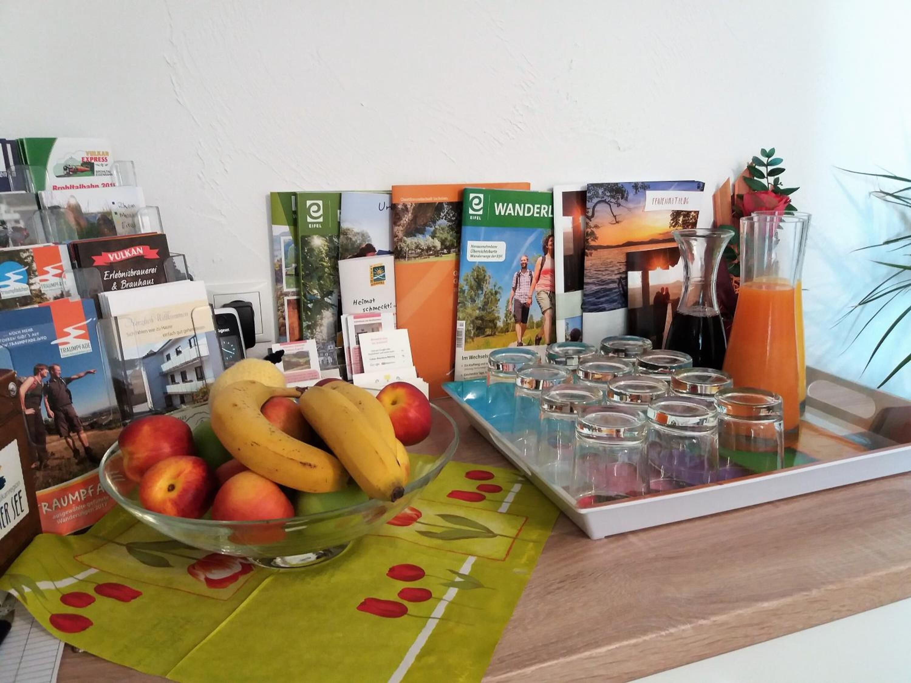 A breakfast setup with a fruit bowl, a tray of shot glasses, and a glass of orange juice.