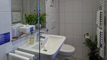A modern bathroom with a large mirror, white tiles, a sink, a toilet, and a potted plant.