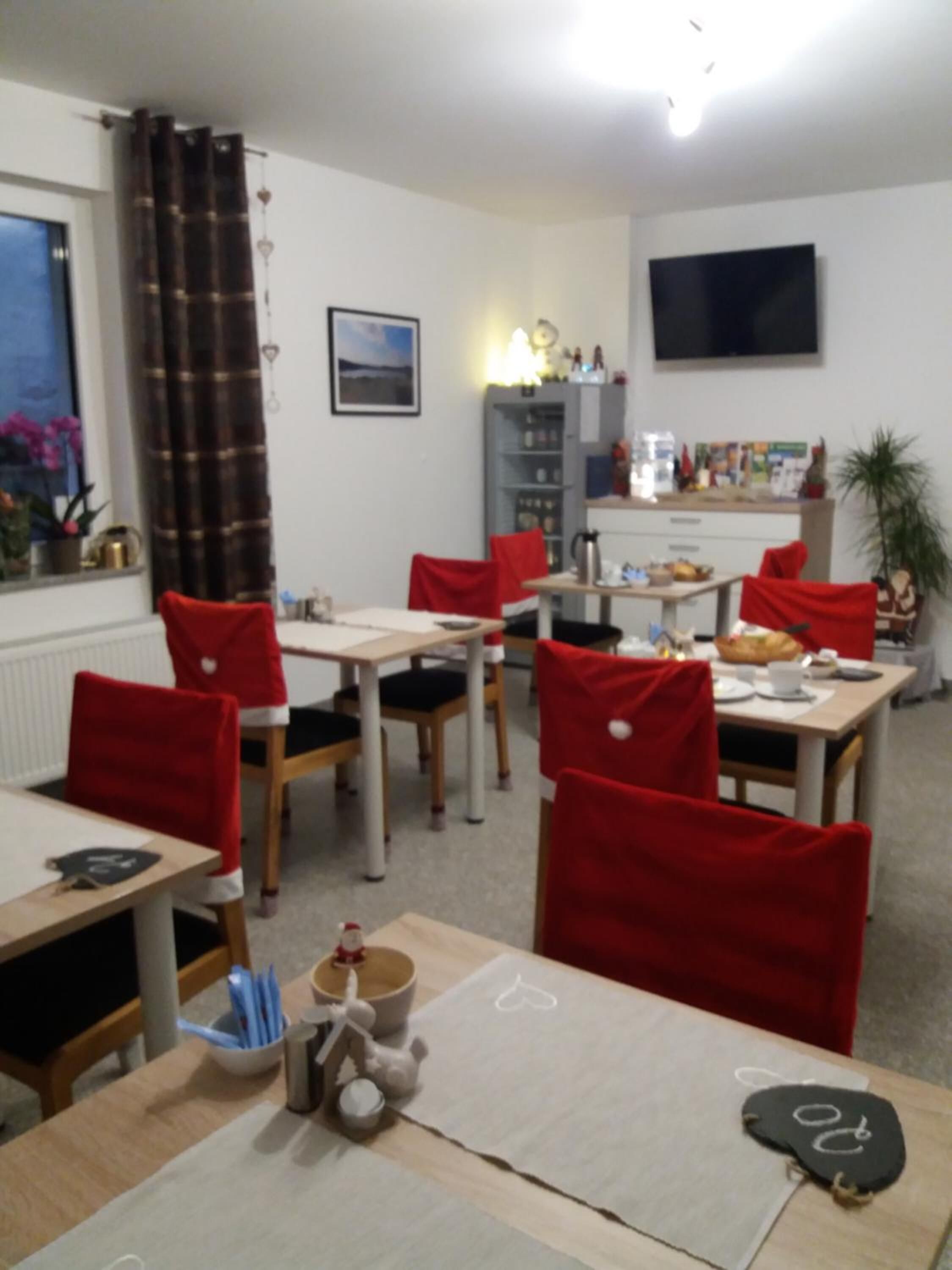Een eetgedeelte met rode stoelen, een tafel met placemat en een aan de muur bevestigde televisie.