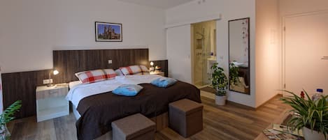 A modern bedroom with a large bed, bedside tables, a nightstand, a mirror, and a potted plant.