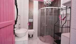 A bathroom with a white sink, a toilet, a shower enclosure, and a pink door. - Kiraz Cicegi Butik Akyaka (Ula)