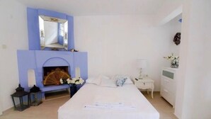 Un dormitorio con chimenea, una cama, una mesita de noche y un aparador.