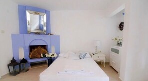 Un dormitorio con chimenea, una cama, una mesita de noche y un aparador.