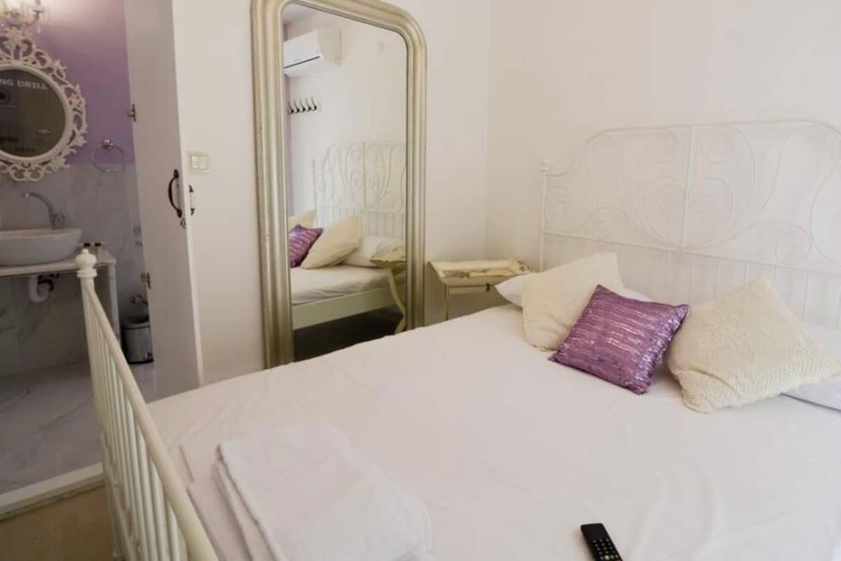 A bed with a headboard, a bedside table, a mirror, and a bathroom with a sink and mirror.
