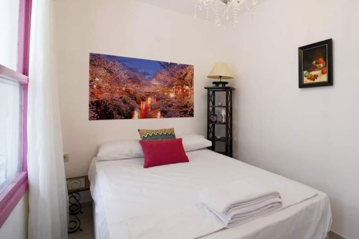 A bedroom with a bed, a nightstand, a lamp, and two wall-mounted pictures.