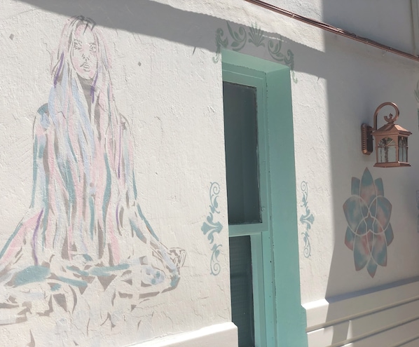 A wall with a mural of a figure, a door, and a lantern. - Kiraz Cicegi Butik Akyaka (Ula)