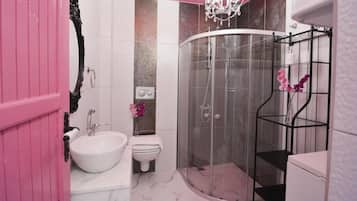 Baño con lavamanos blanco, inodoro, cabina de ducha y puerta rosa.