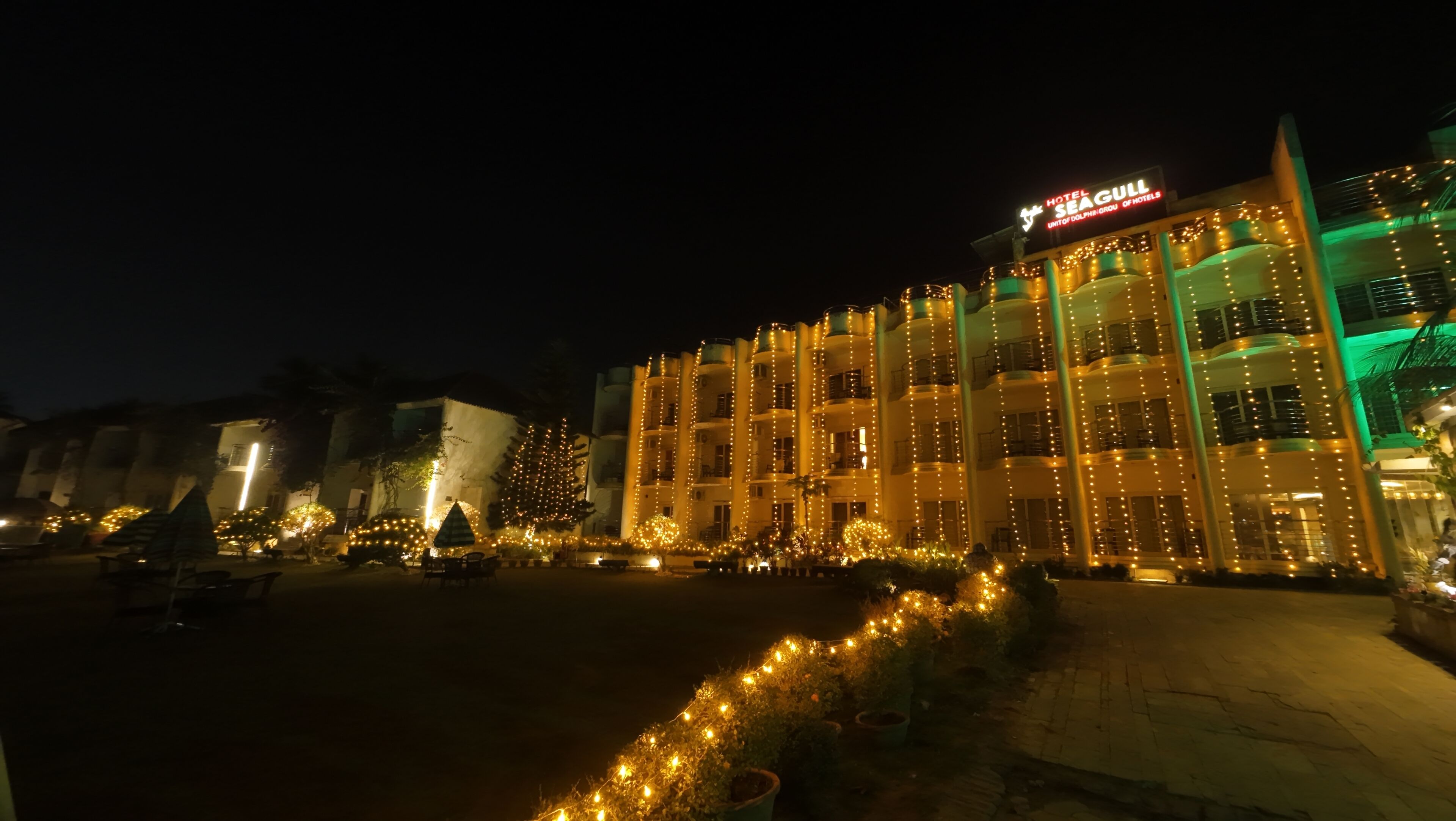 A hotel with multiple balconies, a well-lit entrance, and a sign indicating it is part of the Dolphin Group of Hotels.