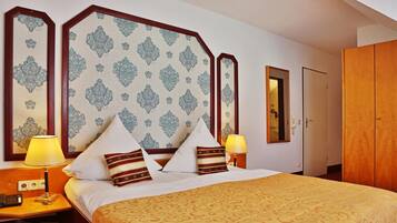 A hotel room with a large bed, two bedside lamps, a wooden wardrobe, and a mirror on the wall.