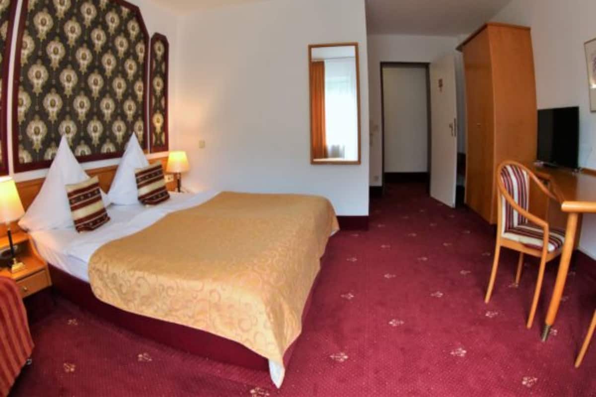 A hotel room with a bed, bedside tables, a desk, a chair, a mirror, and a wardrobe.
