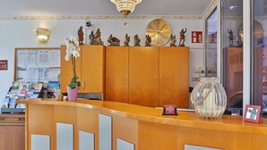 A hotel reception area with a wooden counter, a large clock, and various decorative items including figurines and a vase. - Hotel Neckarlux (Heidelberg)