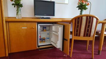 Una kitchenette compacta con refrigerador, un televisor pequeño y una silla.
