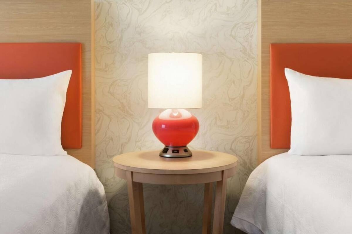 Une chambre d’hôtel avec deux lits, une table ronde surmontée d’une lampe rouge et un papier peint à motifs.