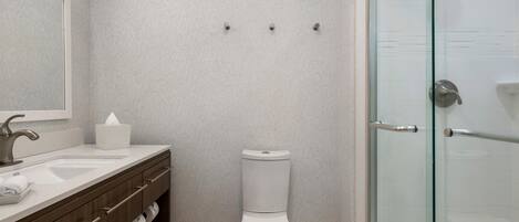 A bathroom with a white sink, mirror, toilet, and glass shower enclosure.