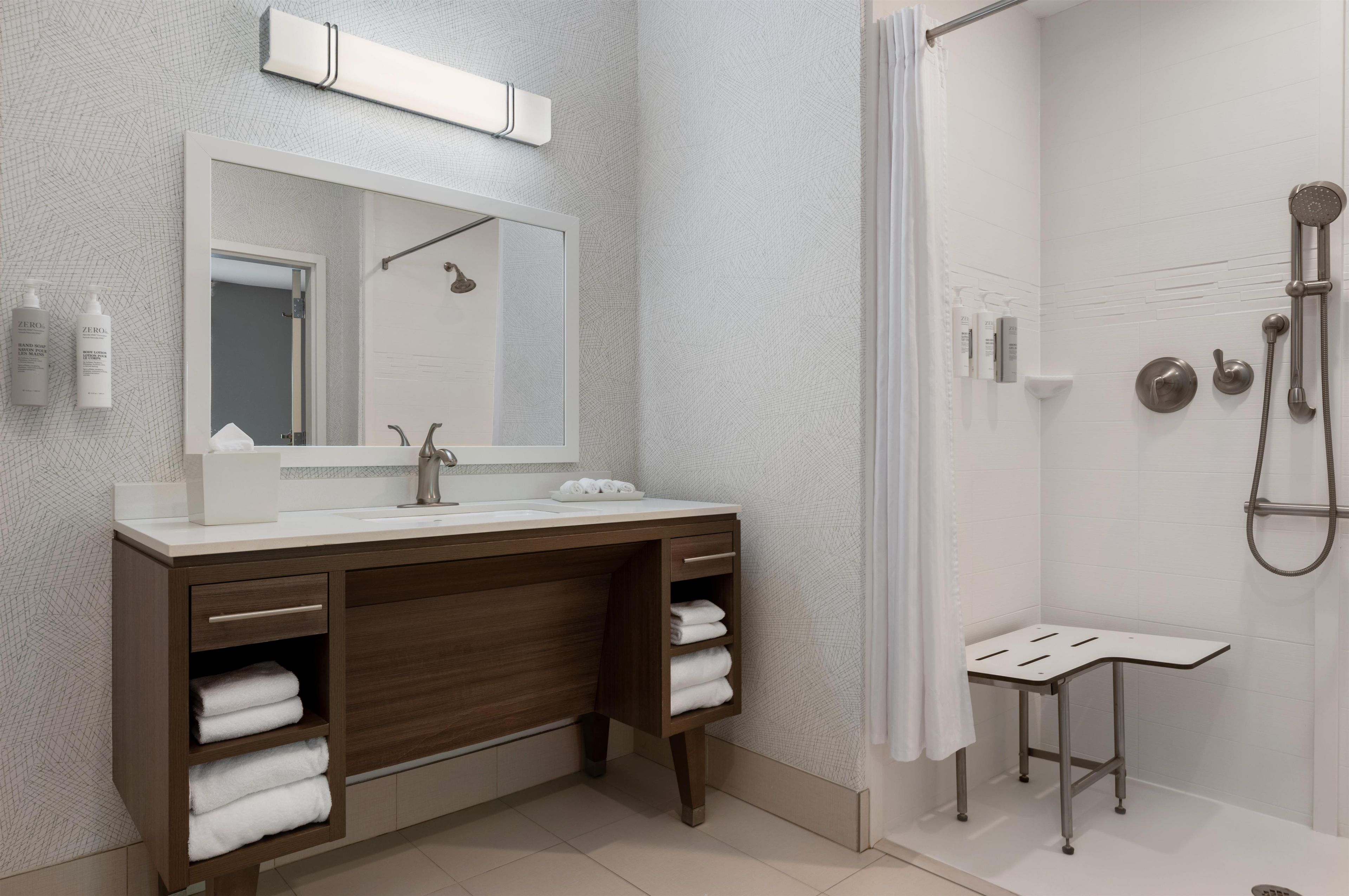 A modern bathroom with a large mirror, dual sinks, a shower, and a small table.
