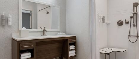 A modern bathroom with a large mirror, dual sinks, a shower, and a small table.