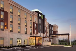 A multi-story hotel with a prominent 'HOME 2' sign, a covered entrance with seating, and a parking area with handicapped accessibility.