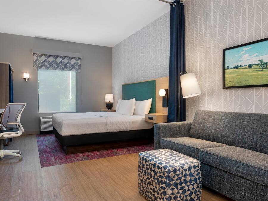 Habitación de hotel con cama, escritorio, silla, sofá y un cuadro en la pared.