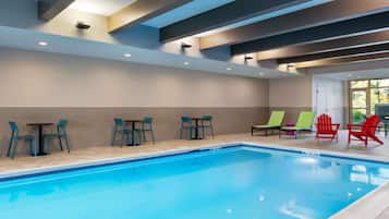 An indoor swimming pool with seating and tables, a tiled floor, and a ceiling with recessed lighting.