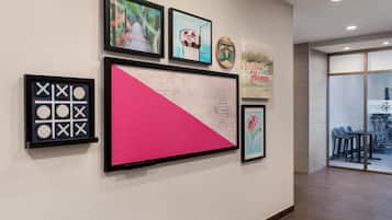 A wall with framed artwork, a large pink and white geometric piece, and a welcome sign.