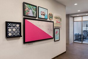A wall with framed artwork, a large pink and white geometric piece, and a welcome sign. - Home2 Suites Florence/Cincinnati Airport South, KY (Florence)